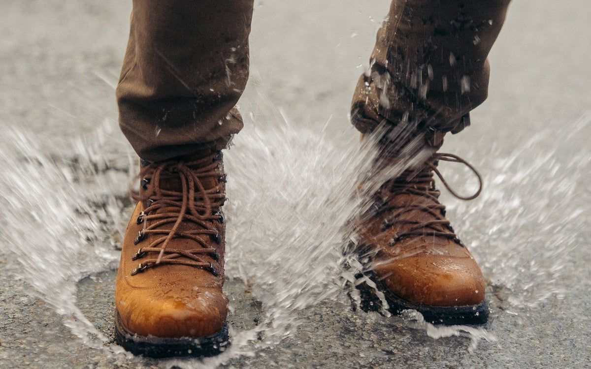 Tan leather winter boots splashing through a puddle on a wet road