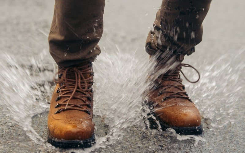 Tan leather winter boots splashing through a puddle on a wet road