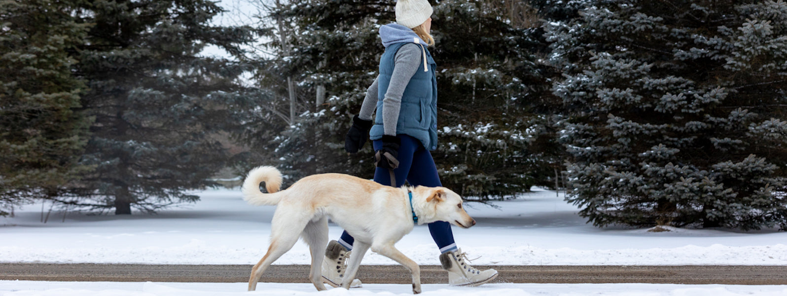 woman walking her dog through the snow in winter boots