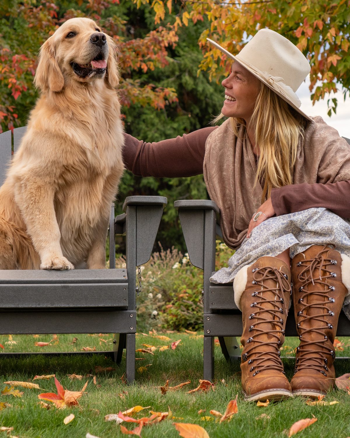 A woman in DALHOUSIE Sunset Wheat boots on an Adirondack chair beside a golden retriever in the fall